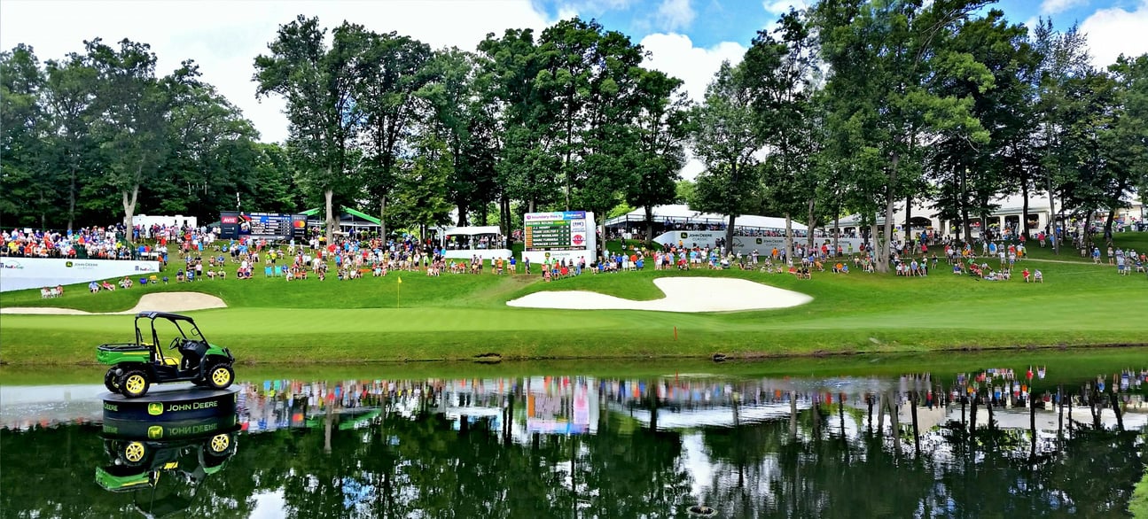 charity tournament at a golf course with people on the green and a golf cart on a stand in the water