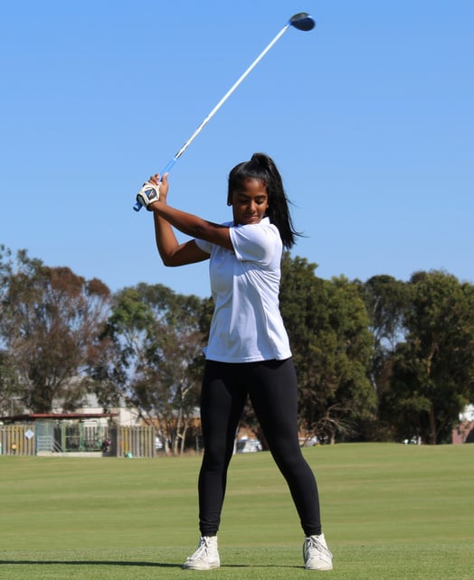 a female in a white shirt and black leggings swinging a golf club